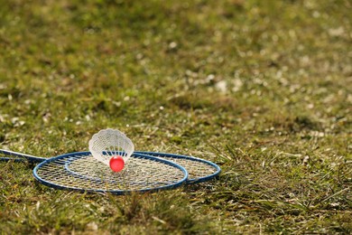 Photo of Badminton racquets and shuttlecock on green grass outdoors. Space for text