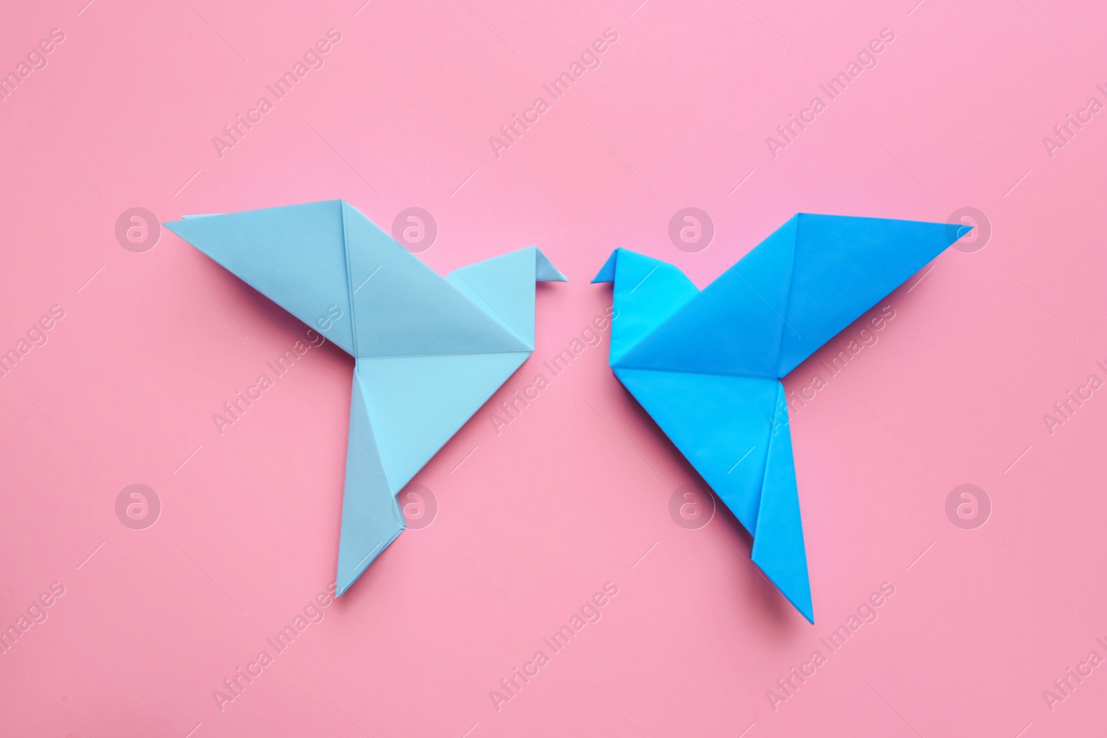 Photo of Beautiful light blue origami birds on pink background, flat lay