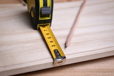Tape measure and pencil on wooden surface, closeup