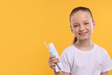 Happy girl holding electric toothbrush and tube of toothpaste on yellow background. Space for text