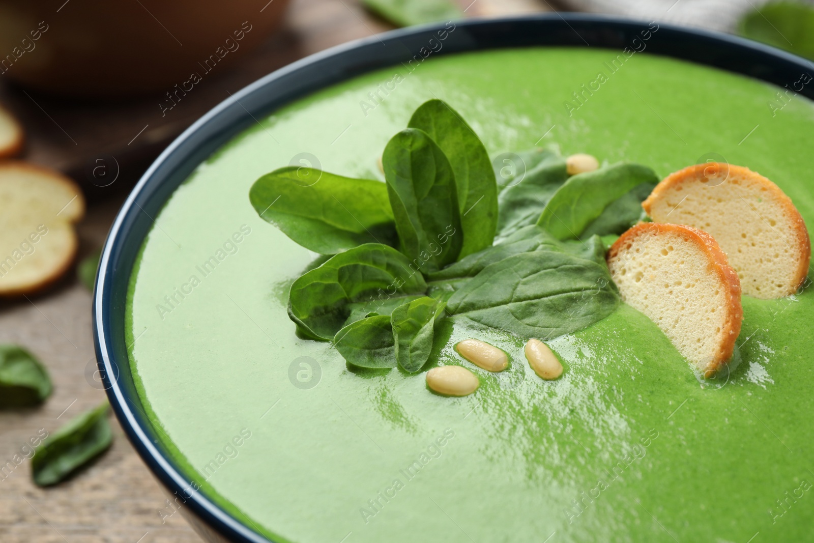 Photo of Bowl of healthy green soup with fresh spinach on wooden table, closeup view