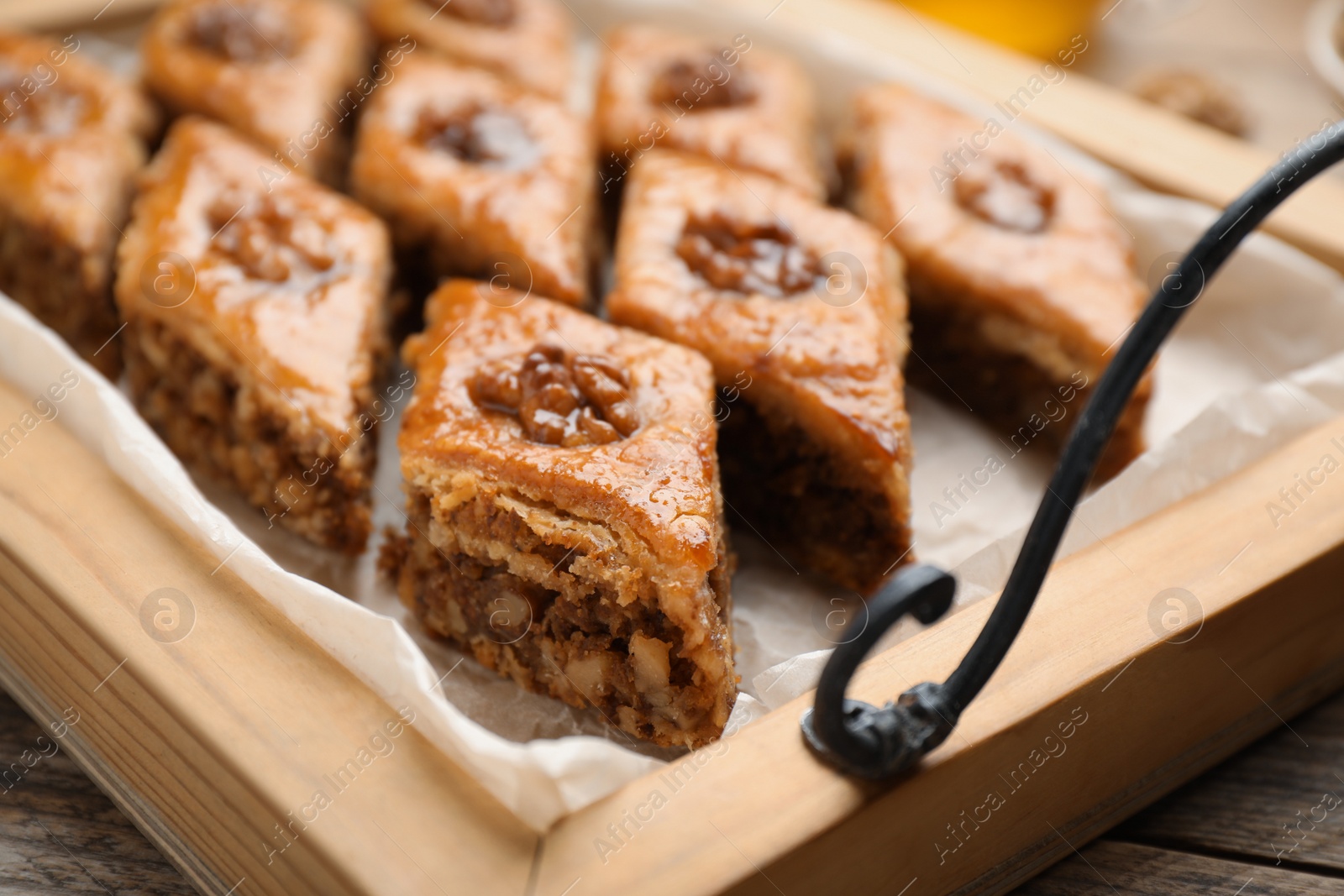 Photo of Delicious honey baklava with walnuts on wooden tray, closeup