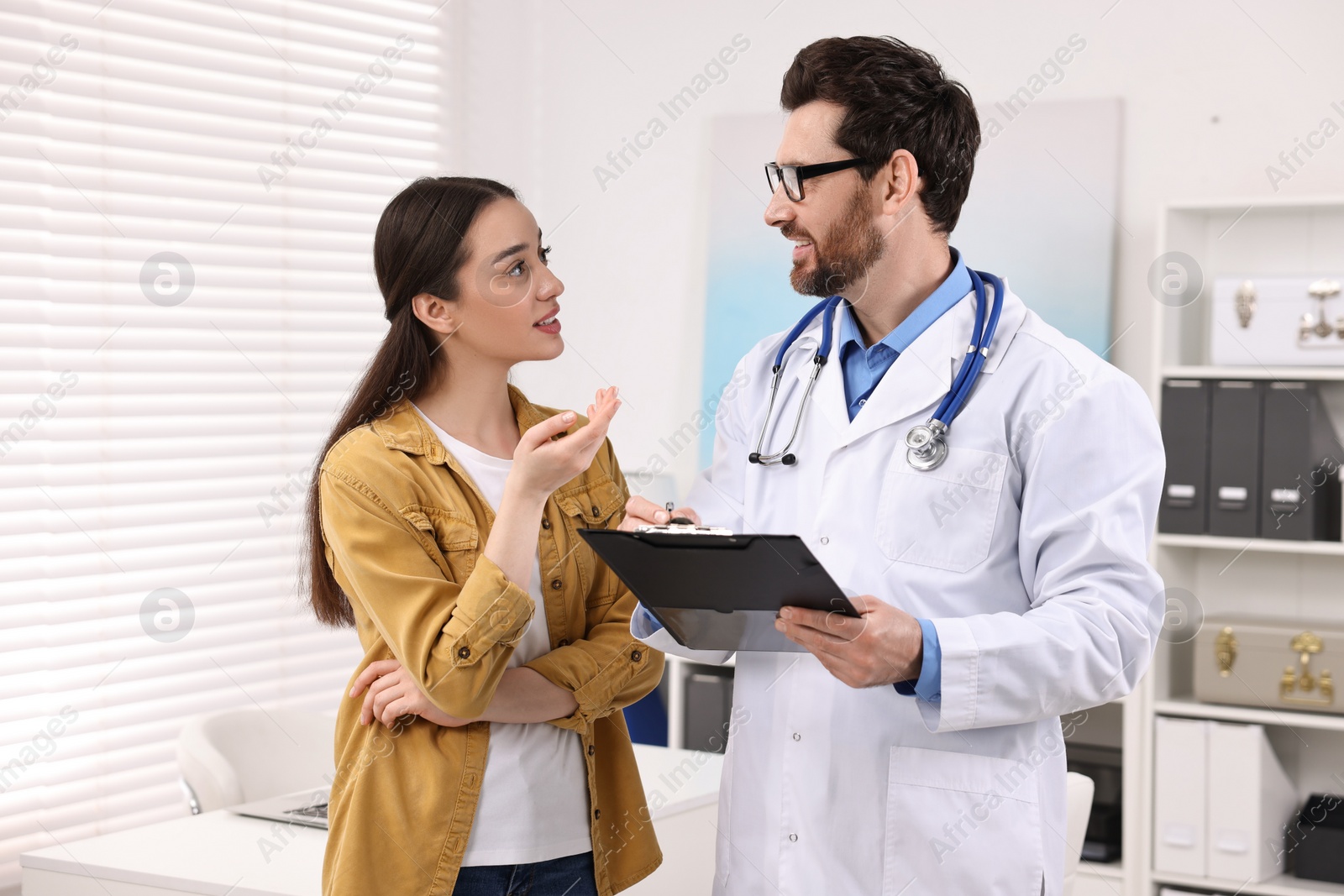 Photo of Doctor with clipboard consulting patient during appointment in clinic