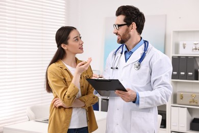 Photo of Doctor with clipboard consulting patient during appointment in clinic