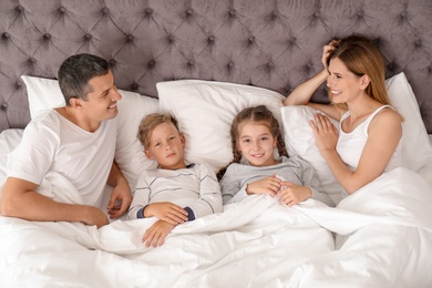 Photo of Couple with children lying under blanket in bed. Happy family