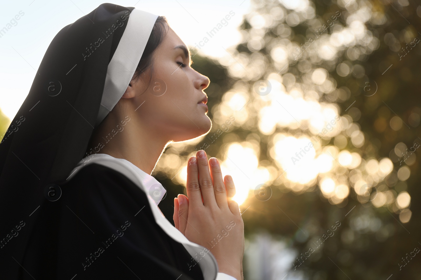 Photo of Young nun with hands clasped together praying outdoors on sunny day, space for text