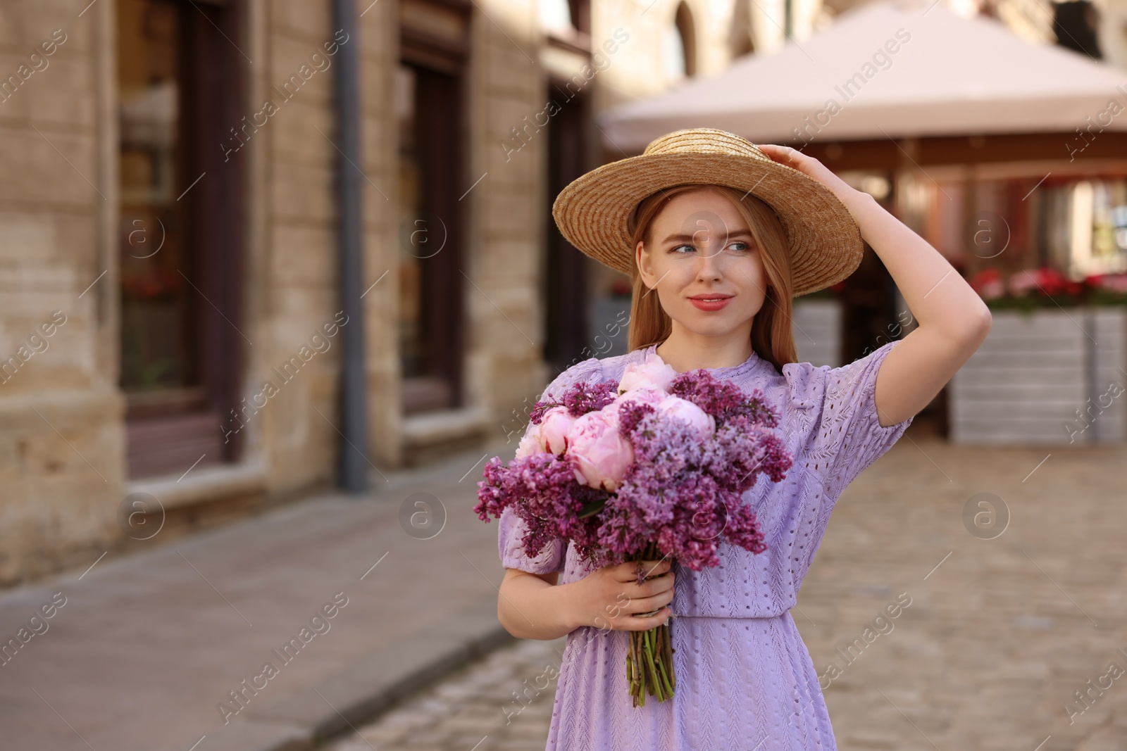 Photo of Beautiful woman with bouquet of spring flowers on city street, space for text