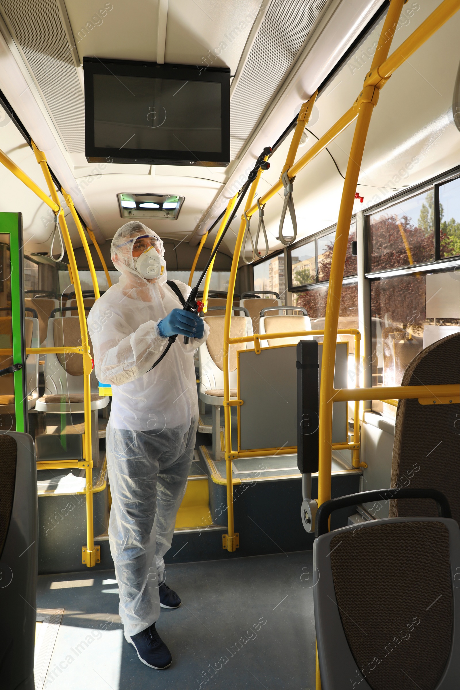 Photo of Public transport sanitation. Worker in protective suit disinfecting bus salon