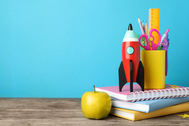 Photo of Bright toy rocket and school supplies on wooden desk. Space for text