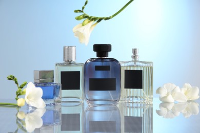 Photo of Luxury perfumes and freesia flowers on mirror surface against light blue background. Floral fragrance