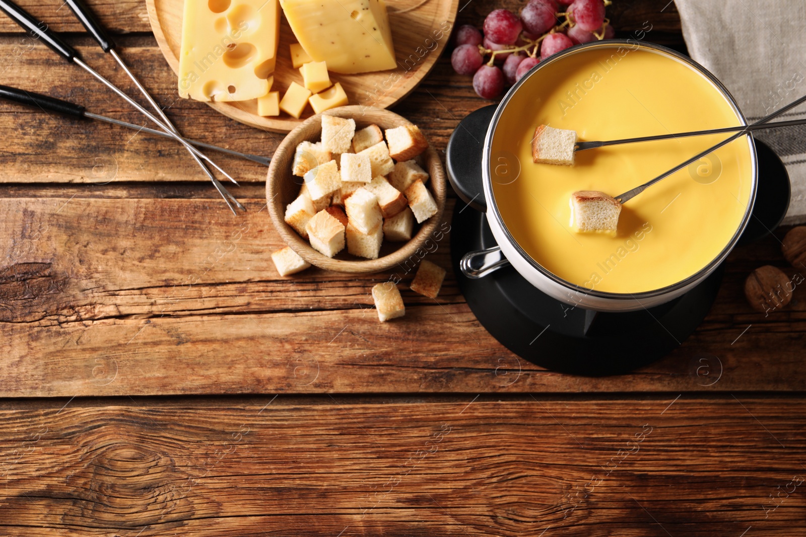 Photo of Pot of tasty cheese fondue and snacks on wooden table, flat lay. Space for text