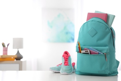 Photo of Bright backpack with different stationery and sport shoes on white table indoors. Space for text