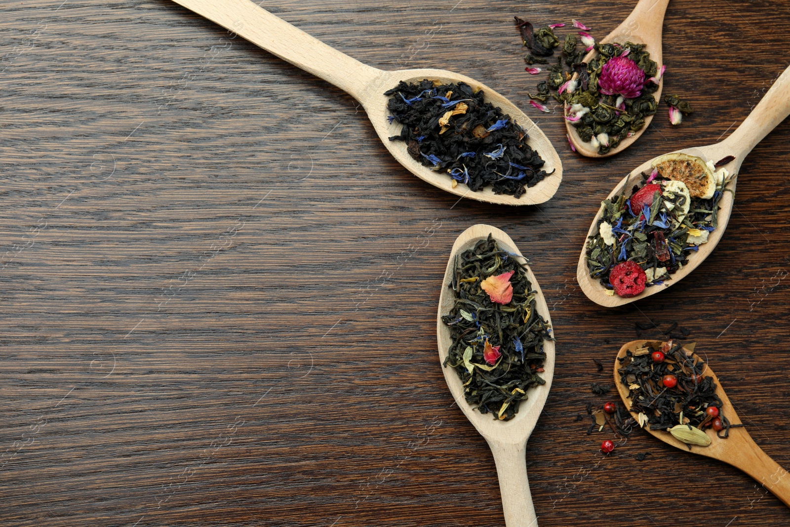 Photo of Flat composition with spoons of dried herbal tea leaves on wooden table. Space for text