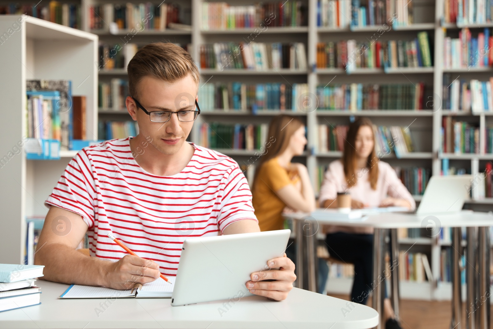 Photo of Young man studying with tablet at table in library. Space for text