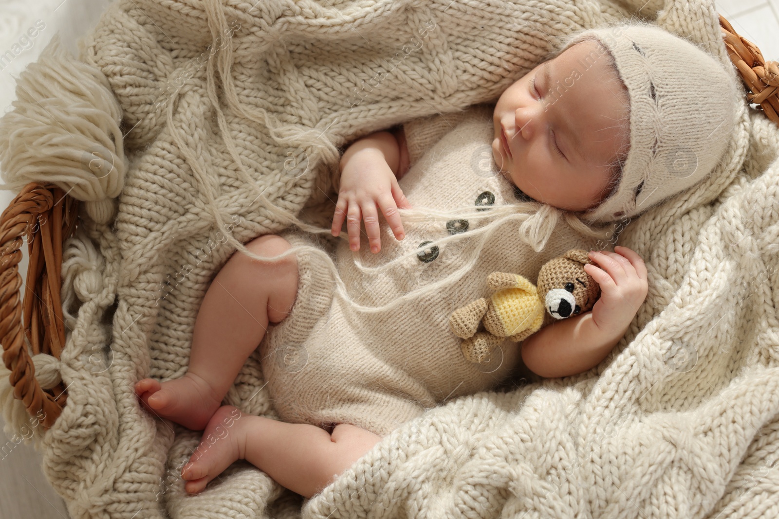 Photo of Adorable newborn baby with toy bear sleeping in wicker basket, top view