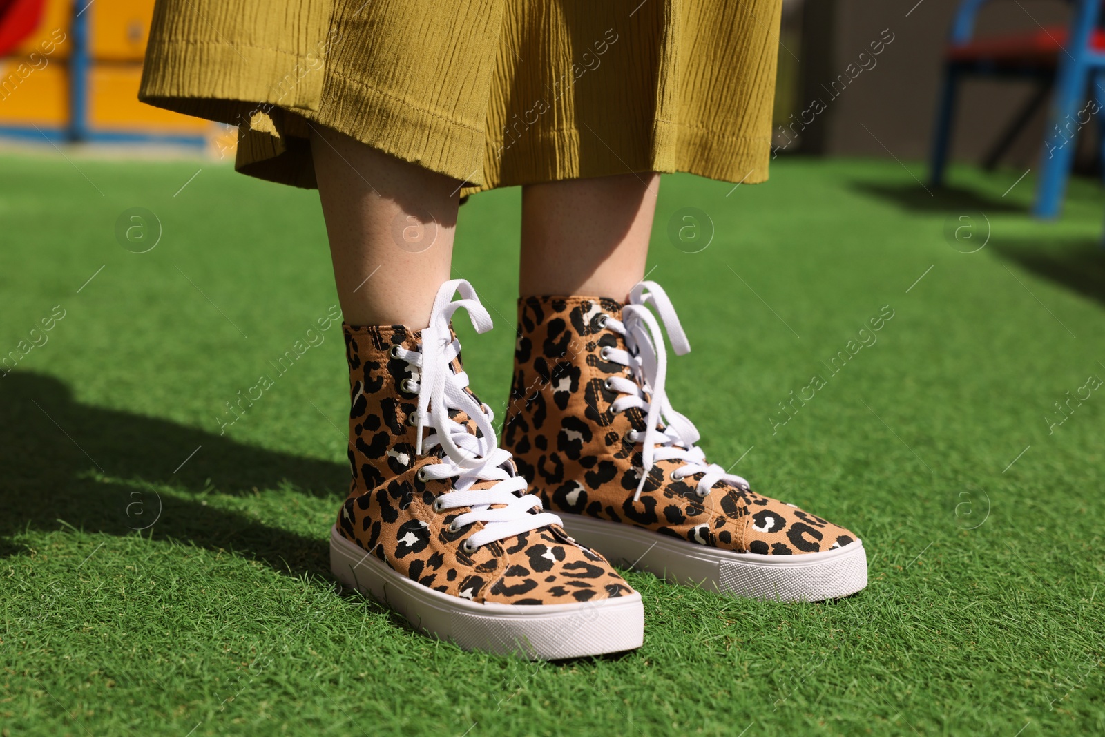 Photo of Woman wearing sneakers with leopard print on green grass outdoors, closeup