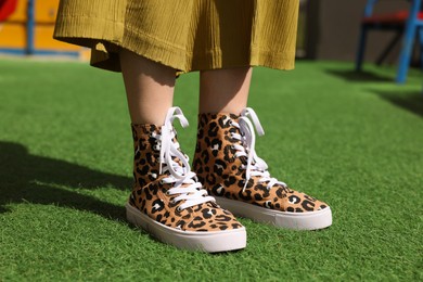 Photo of Woman wearing sneakers with leopard print on green grass outdoors, closeup