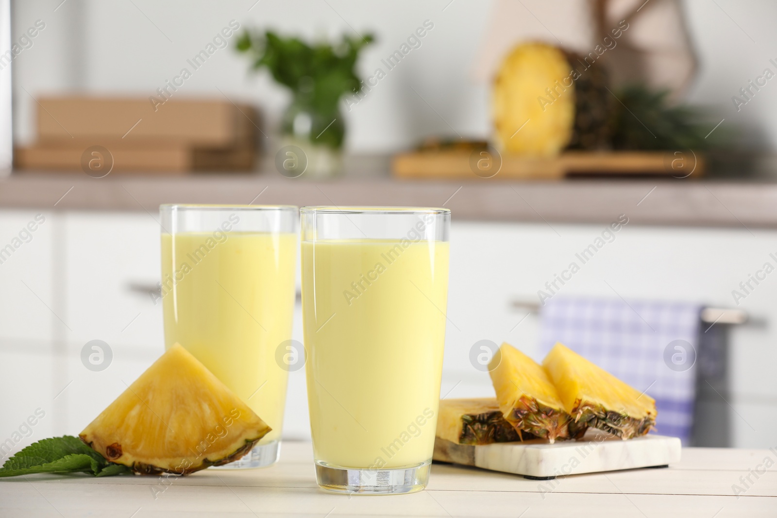 Photo of Glasses of tasty pineapple smoothie, mint and cut fruit on white table indoors