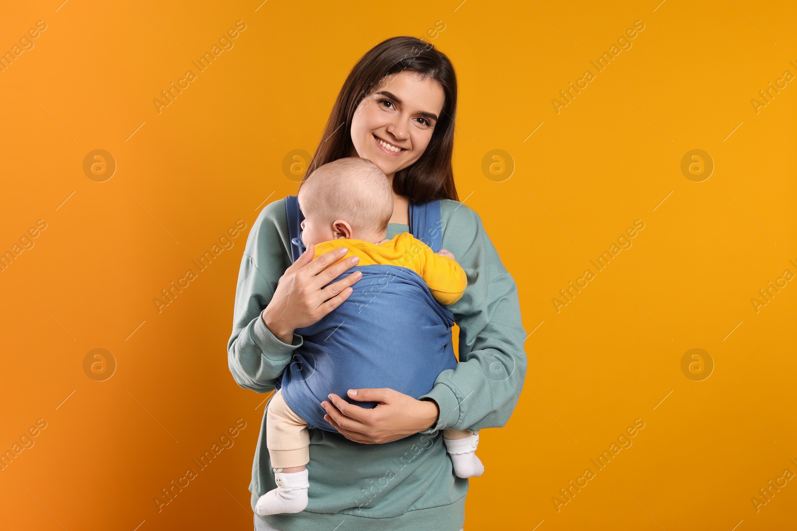 Photo of Mother holding her child in sling (baby carrier) on orange background