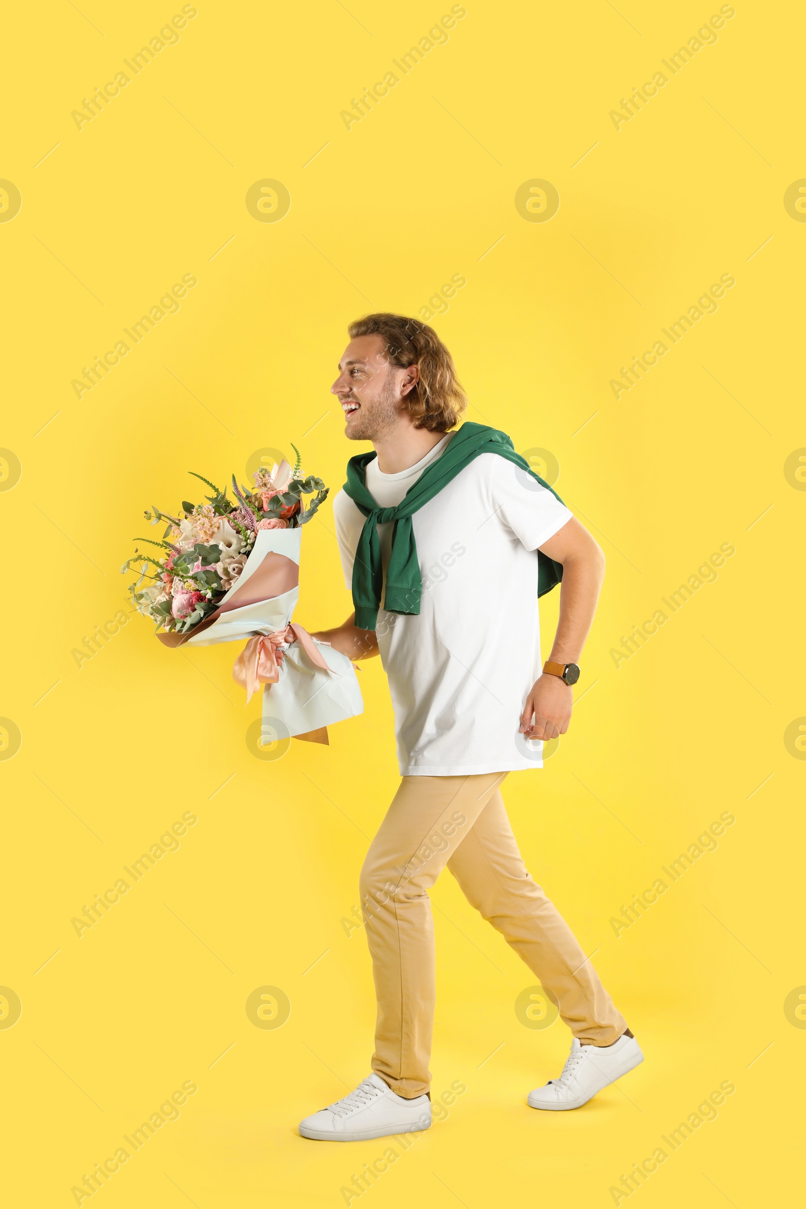 Photo of Young handsome man with beautiful flower bouquet on yellow background