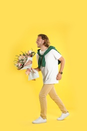 Young handsome man with beautiful flower bouquet on yellow background