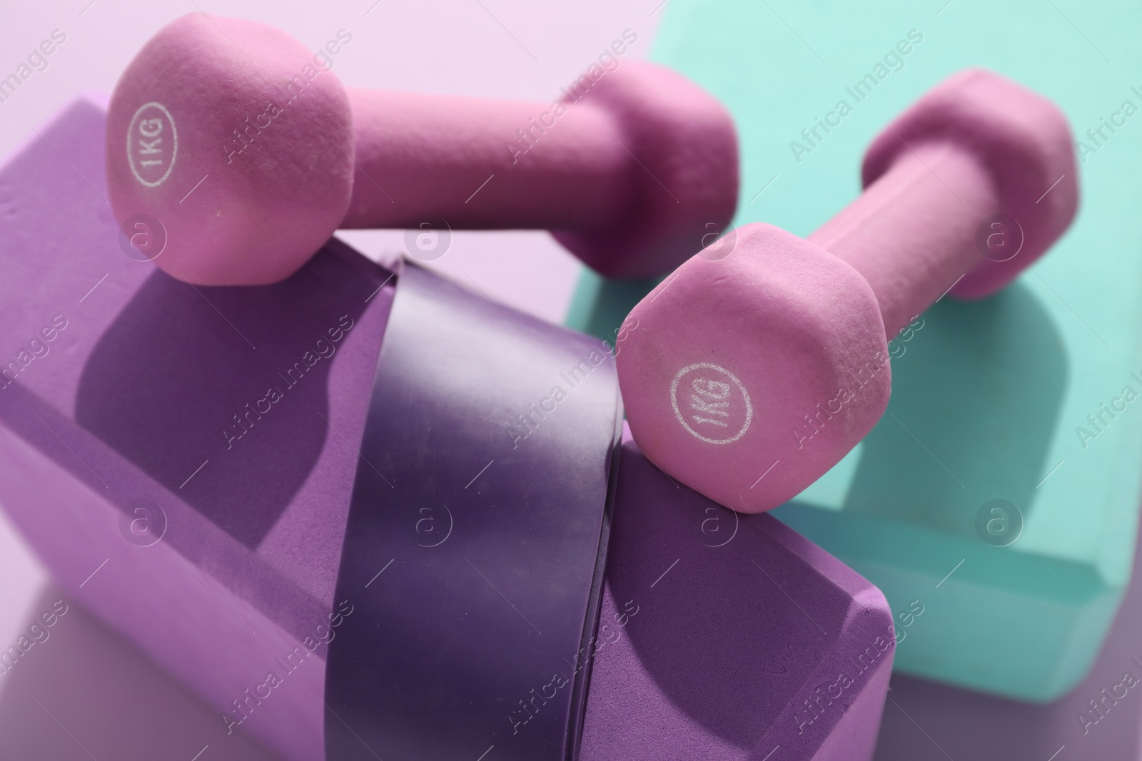 Photo of Two dumbbells, yoga blocks and fitness elastic band on violet background, closeup