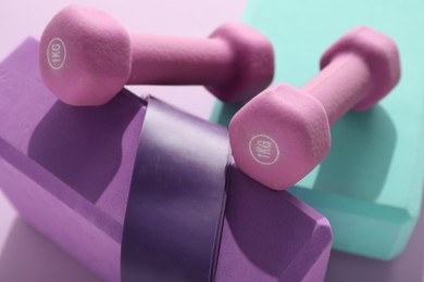 Two dumbbells, yoga blocks and fitness elastic band on violet background, closeup