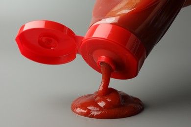 Pouring tasty red ketchup from bottle on light grey background, closeup