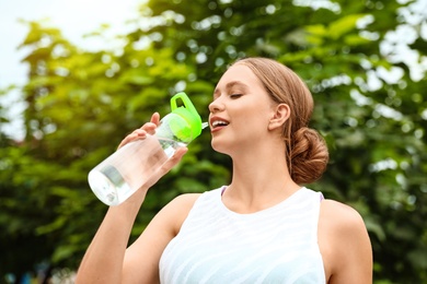 Photo of Young woman drinking water outdoors. Refreshing drink