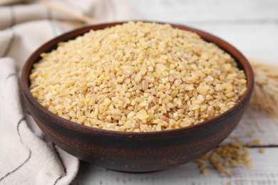 Photo of Raw bulgur in bowl on white wooden table, closeup