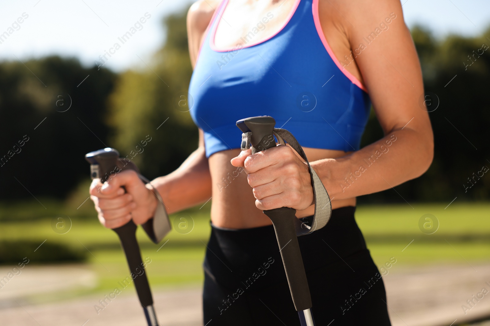 Photo of Woman practicing Nordic walking with poles outdoors on sunny day, closeup