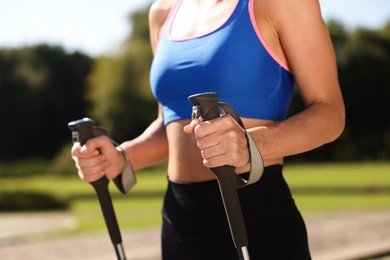 Photo of Woman practicing Nordic walking with poles outdoors on sunny day, closeup