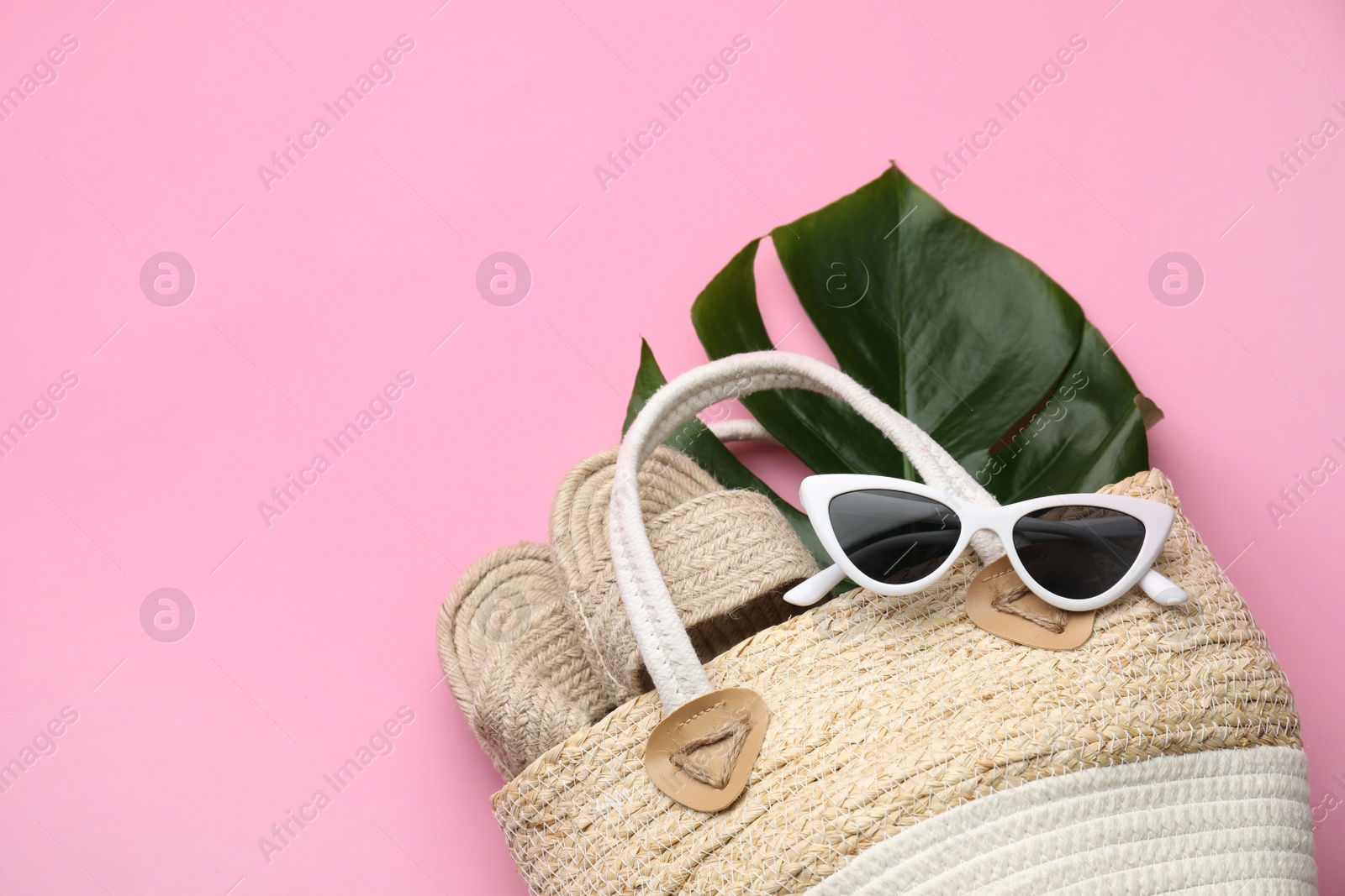 Photo of Elegant woman's straw bag with shoes, tropical leaf and sunglasses on pink background, top view. Space for text