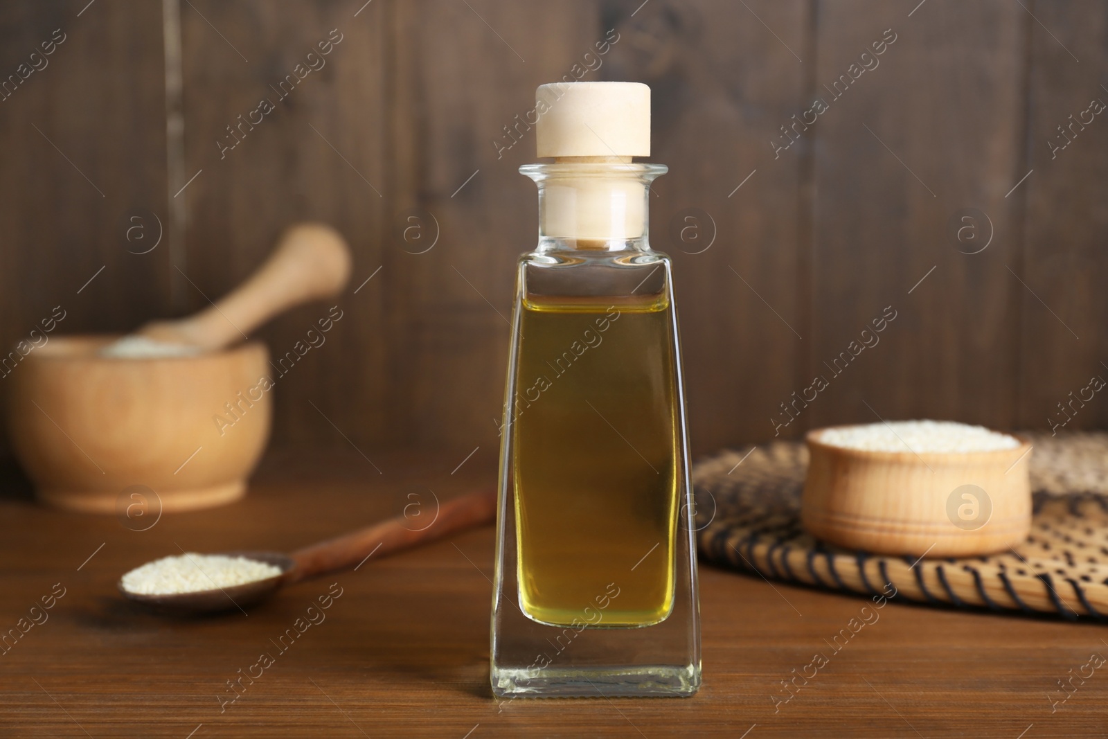 Photo of Fresh sesame oil in glass bottle and seeds on wooden table