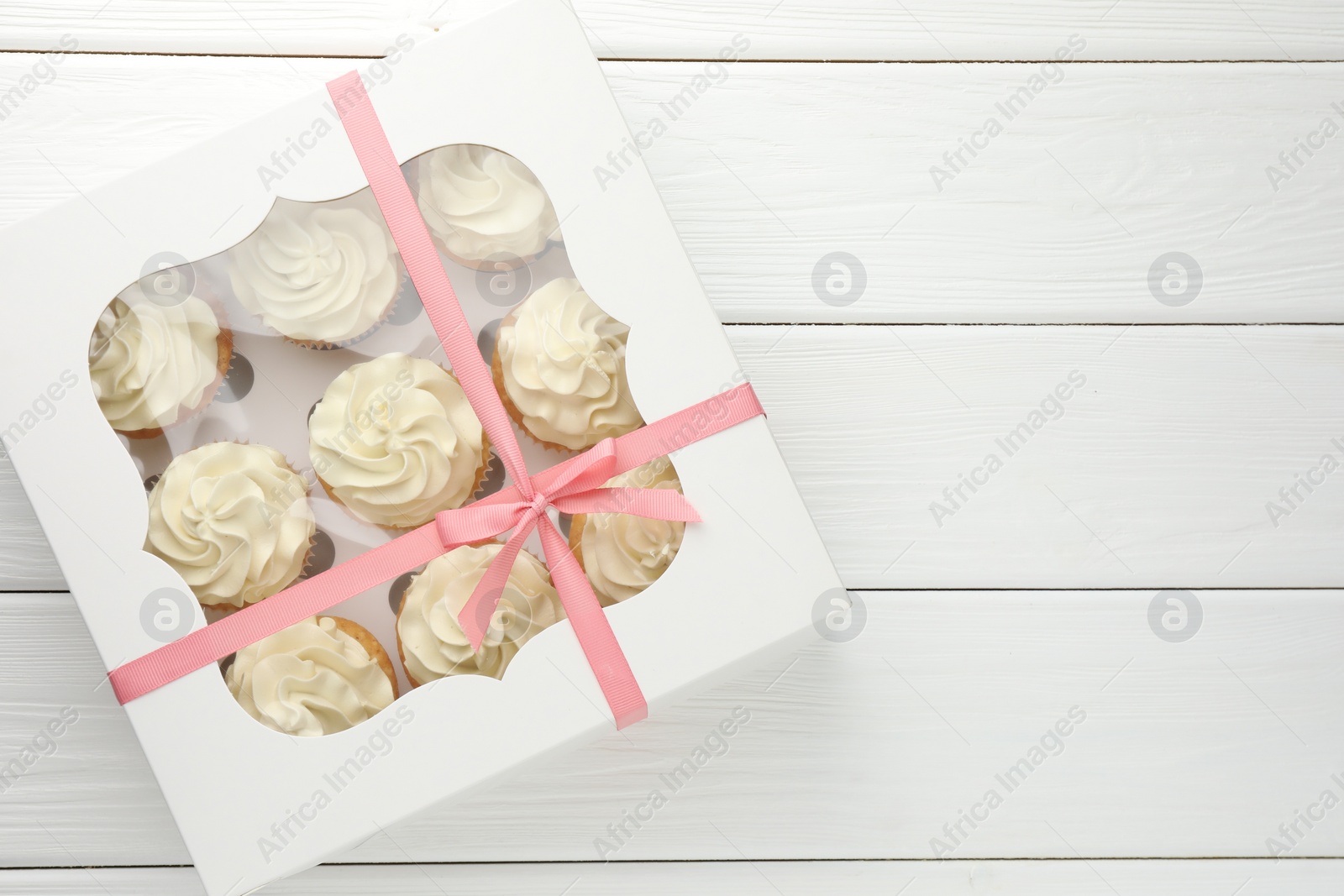 Photo of Tasty cupcakes with vanilla cream in box on white wooden table, top view. Space for text