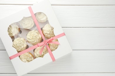 Tasty cupcakes with vanilla cream in box on white wooden table, top view. Space for text