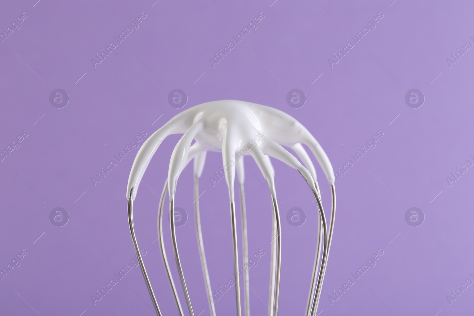 Photo of Whisk with whipped cream on violet background, closeup