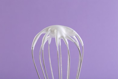 Photo of Whisk with whipped cream on violet background, closeup