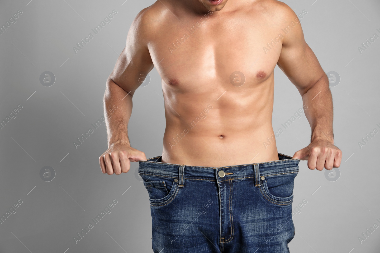 Photo of Young man with slim body in old big size jeans on grey background, closeup view. Space for text