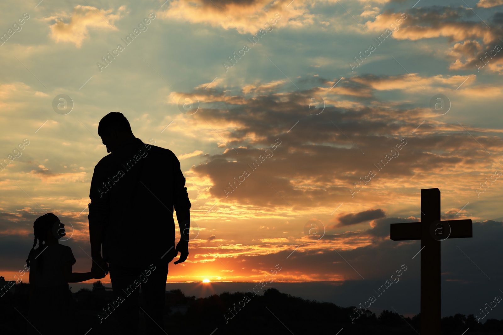 Image of Silhouettes of godparent with child in field at sunset