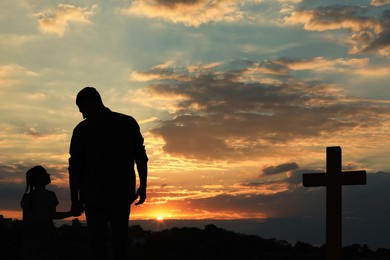 Silhouettes of godparent with child in field at sunset