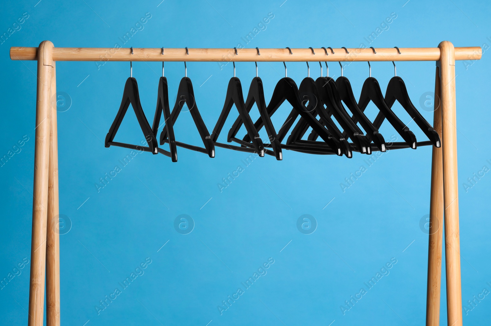 Photo of Black clothes hangers on wooden rack against light blue background