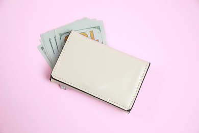 Photo of Stylish leather purse and dollar banknotes on pink background, above view