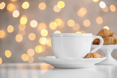 Photo of Cup of drink and pastry on table against blurred lights, space for text