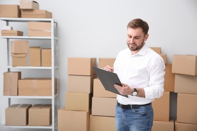 Photo of Young businessman with clipboard near cardboard boxes at warehouse