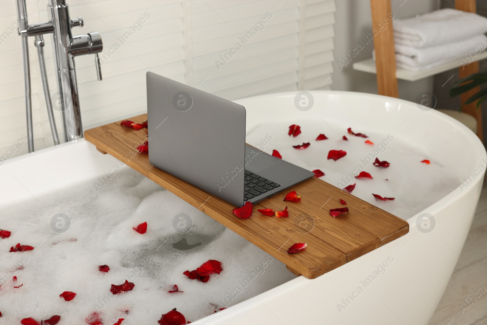 Photo of Wooden board with laptop and rose petals on bath tub