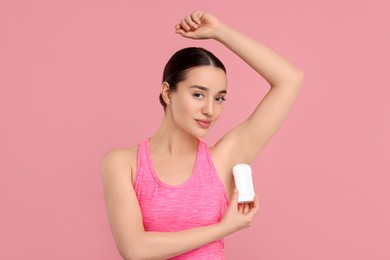 Beautiful woman applying deodorant on pink background