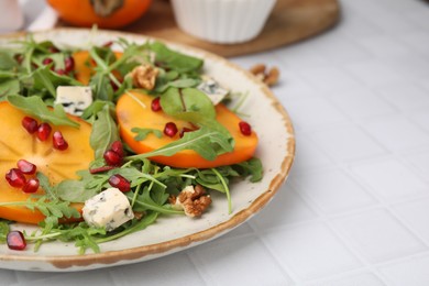 Photo of Tasty salad with persimmon, blue cheese, pomegranate and walnuts served on white tiled table, closeup. Space for text