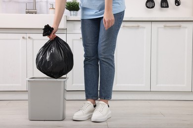 Photo of Woman taking garbage bag out of trash bin in kitchen, closeup