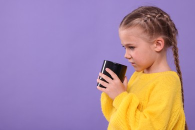 Cute girl with black ceramic mug on violet background, space for text